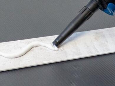 Applying construction adhesive to the back of a skirting board before fixing it securely to a wall.