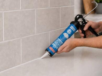 Applying silicone sealant along the joint between a tiled wall and countertop to create a waterproof seal.