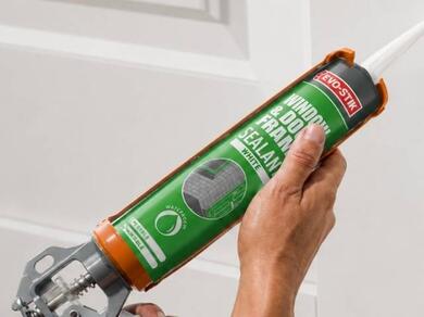 Applying white sealant to a door frame with a sealant gun for a clean finish.