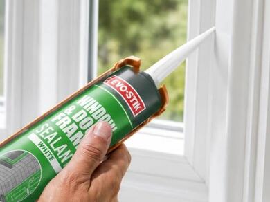 Applying white window and door frame sealant around a uPVC window frame to create a weatherproof and draft-resistant seal.