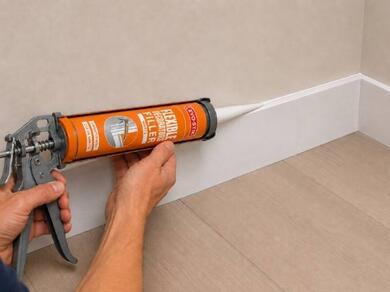 Applying decorators caulk along the top edge of a skirting board to create a smooth, paint-ready finish between the wall and trim.
